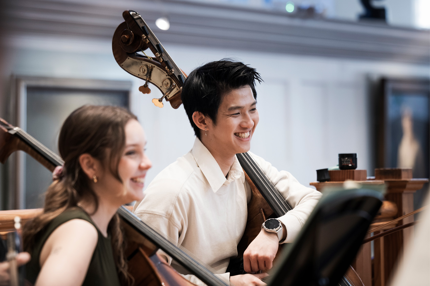 Double bassists smiling while holding their double basses, in an orchestra rehearsal.